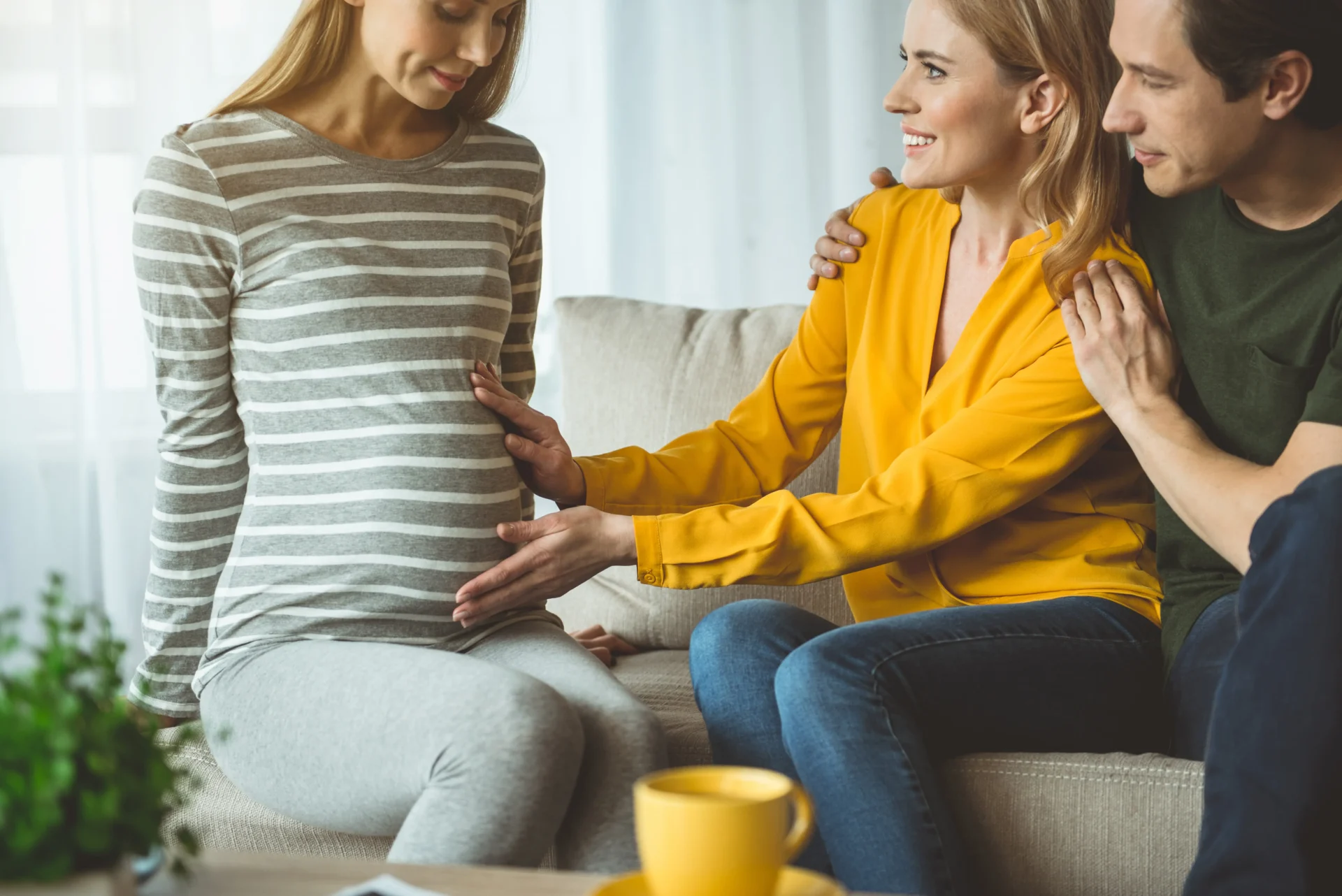 A couple sit on a sofa and place their hands on a pregnant woman's stomach.