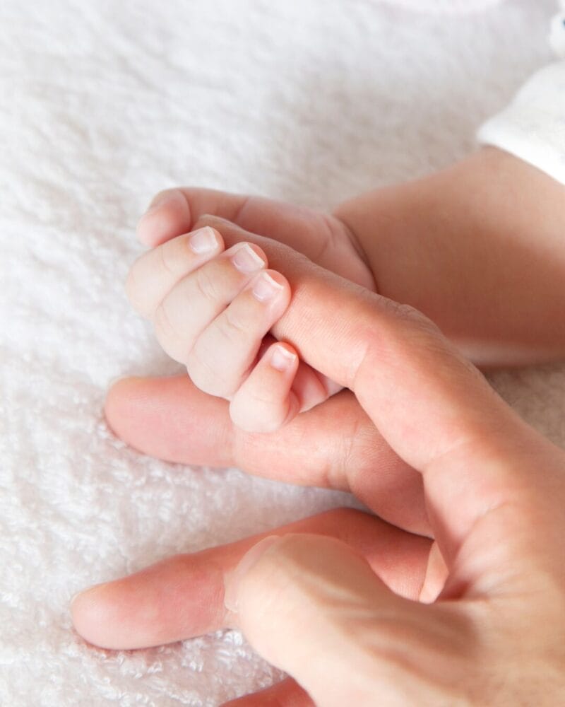 A baby clasps their mother's index finger.