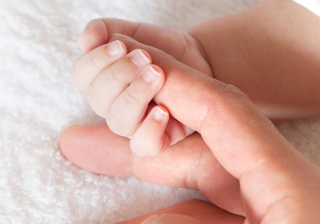 A baby clasps their mother's index finger.