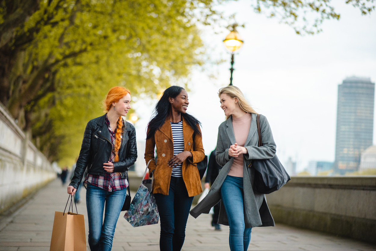 Close up view of attractive young women in winter coats walking in London with shopping bags Diverse group of young adult women with shopping bags walking in London